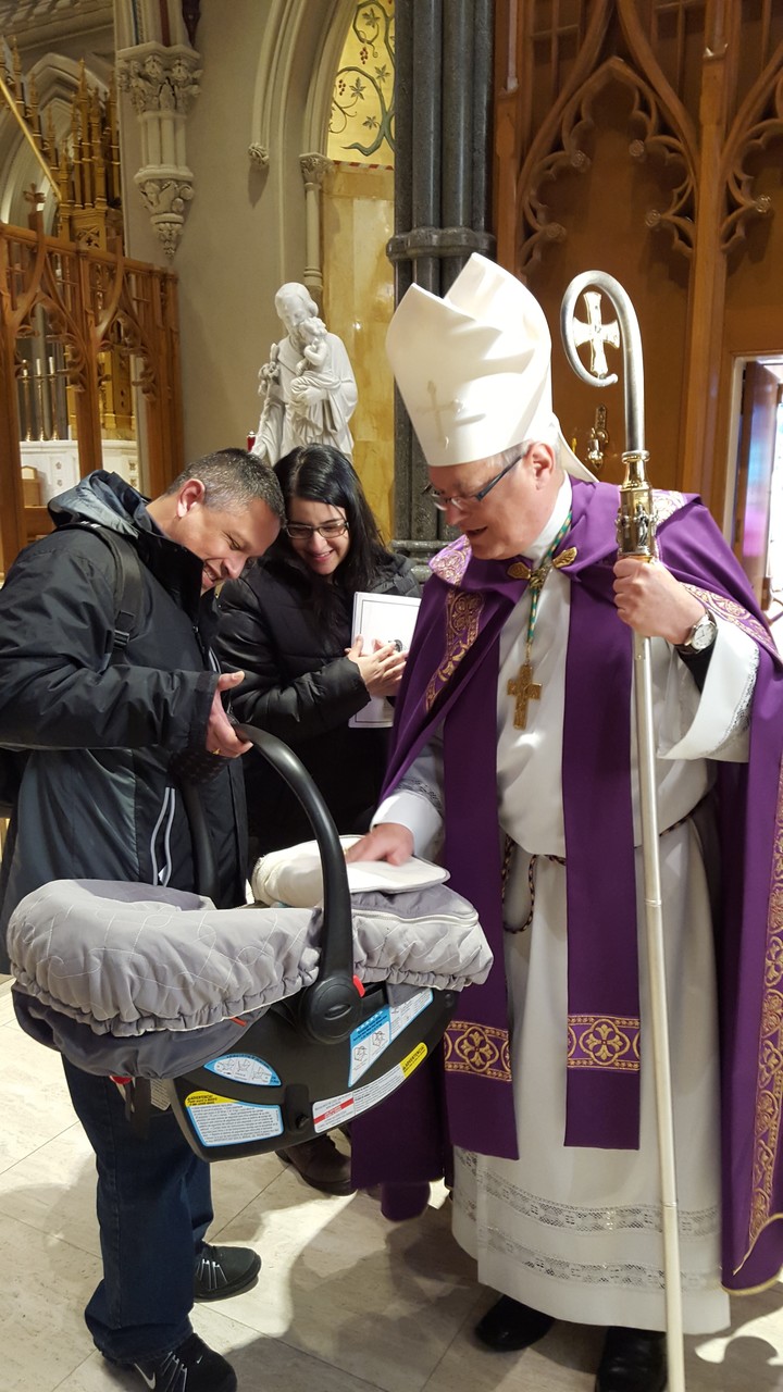 A FAMILY OF GOD: Following the service at the cathedral, Bishop Thomas J. Tobin greets two-month-old Ella Martinez, who is being held by her father, Marty, while mom Yanet, a candidate for continuing conversion, looks on.