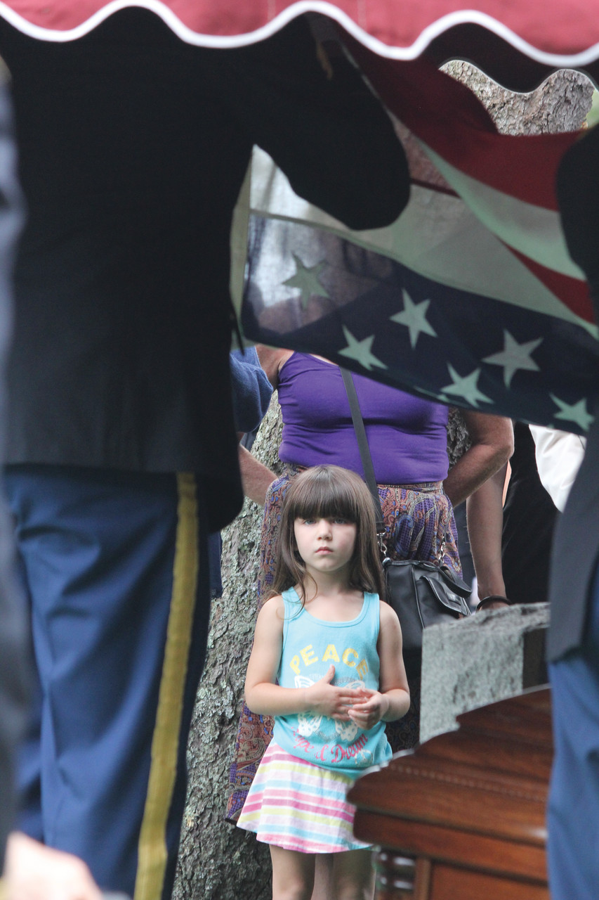 A young girl in attendance holds her hand over her heart as the Honor Guard wraps the flag covering the casket before presenting it to the family.