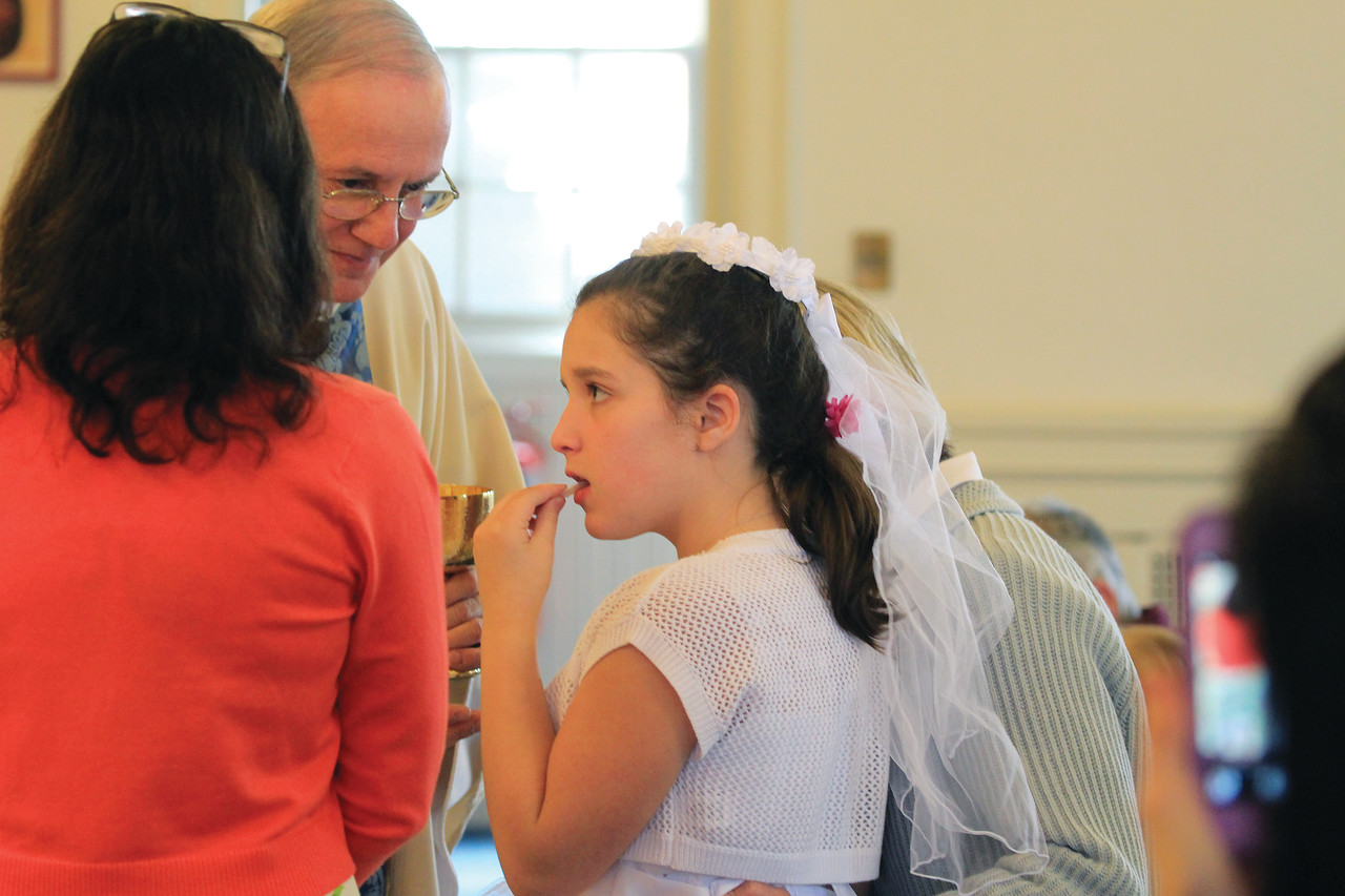 As Father Roger Gagne looks on, Alexis Harnois, a parishioner of St. Joseph Church, Pascoag, receives her first Communion as a student in St. Peter Church’s Autism and the Sacraments program.