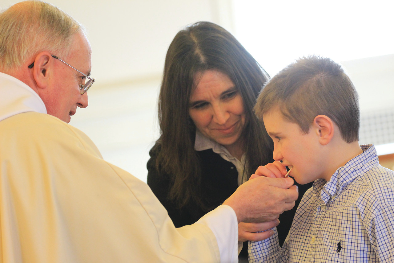 Max Mihalos, a St. Peter, Warwick, parishioner and student in the Autism and the Sacraments faith formation program, receives his first Communion from the pastor, Father Roger Gagne. At right,