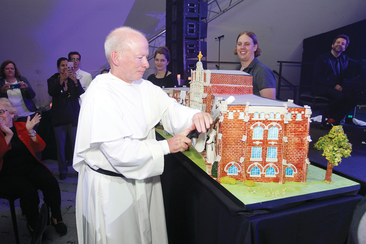 Father Brian Shanley cuts the Centennial cake at Saturday’s St. Dominic Weekend celebration. The finished cake served 800 guests and included more than 100 windows, four fondant figures and 12 layers at its highest point.