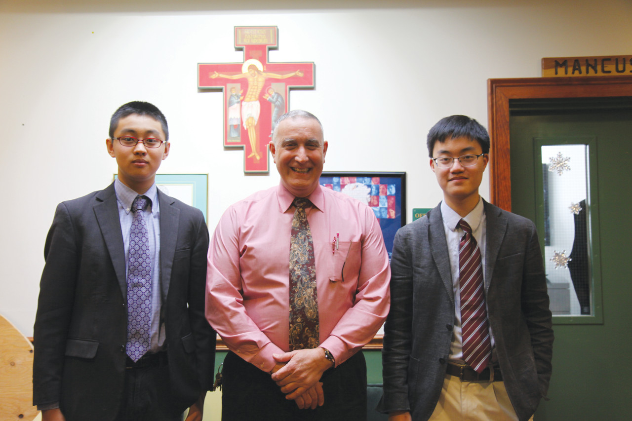 Steve Huang, left, a junior at Bishop Hendricken High School from Beijing, China, and Brandon Lee, a junior from Seoul, Korea, stand with Campus Minister Tom Gambardella in the school’s campus ministry office. Lee, whose country has a strong Catholic presence, says he used to attend Mass with his grandparents, but Huang had almost no familiarity with Catholicism prior to attending Bishop Hendricken.