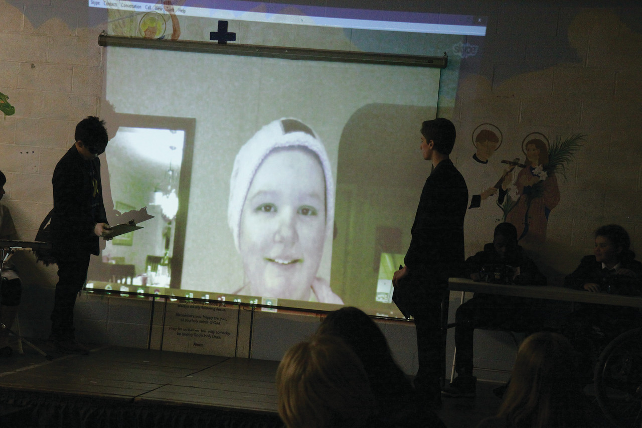 Hannah Skypes with classmates and families during an assembly at the school’s History Night at the Museum. The school has rallied around their missing classmate, theming their projects around childhood cancer and cancer research.