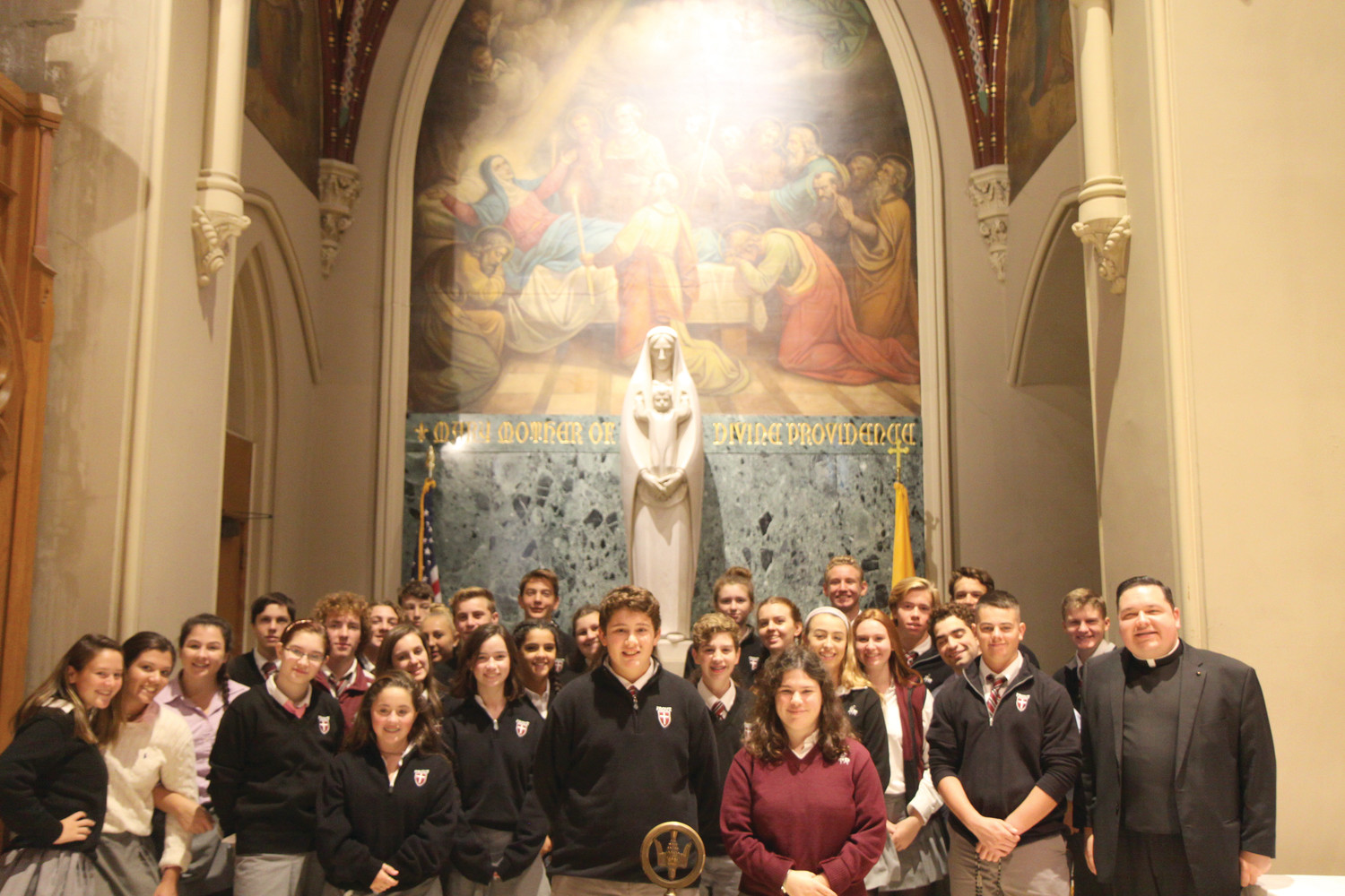 Students, along with Chaplain Father Joseph Upton, pose for a photo before a statue of Our Lady of Providence at the Cathedral of Saints Peter and Paul.