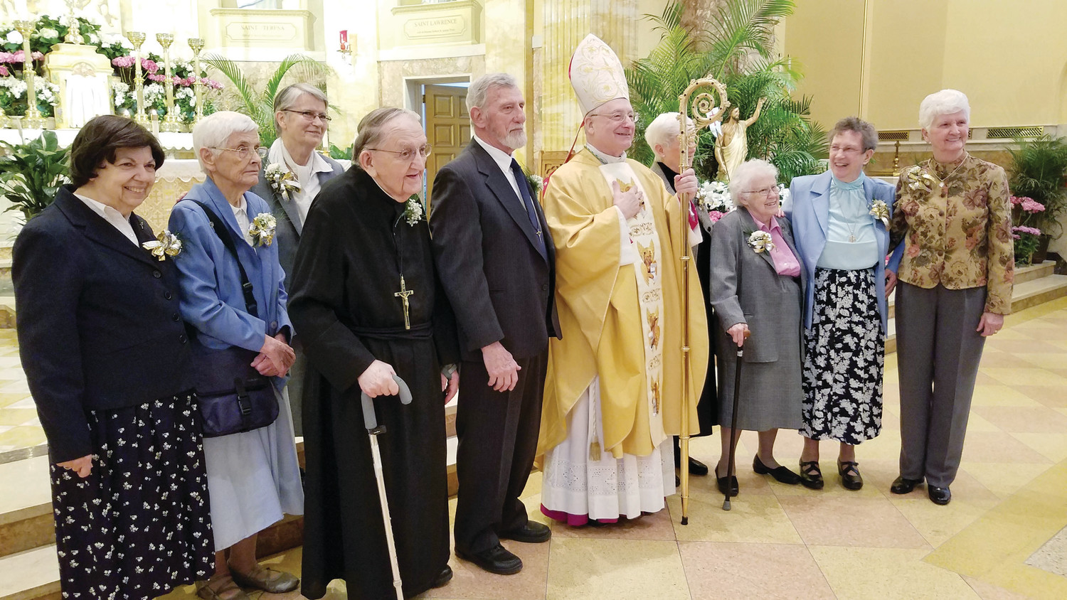 Auxiliary Bishop Robert C. Evans gathers for a photo with some of the jubilarians, including Brother Louis Laperle, who is wearing a black habit and holding a cane. The Brother of the Sacred Heart is celebrating 70 years of profession.