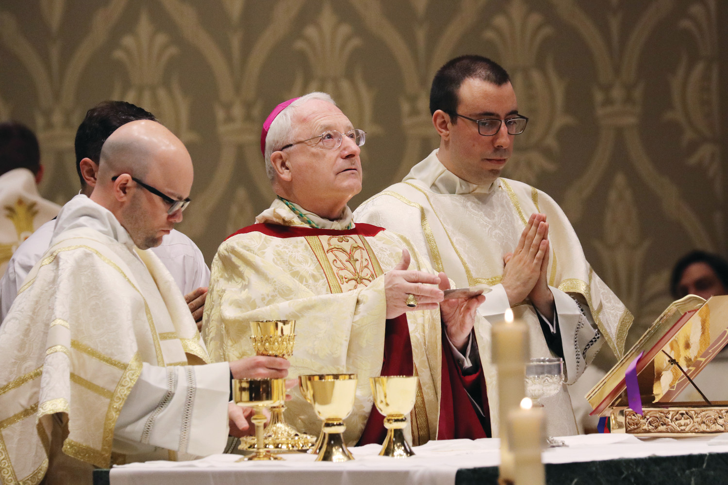 Newly ordained Transitional Deacons Brendan Rowley, left and Eric Silva assist Bishop Robert C. Evans at the altar.