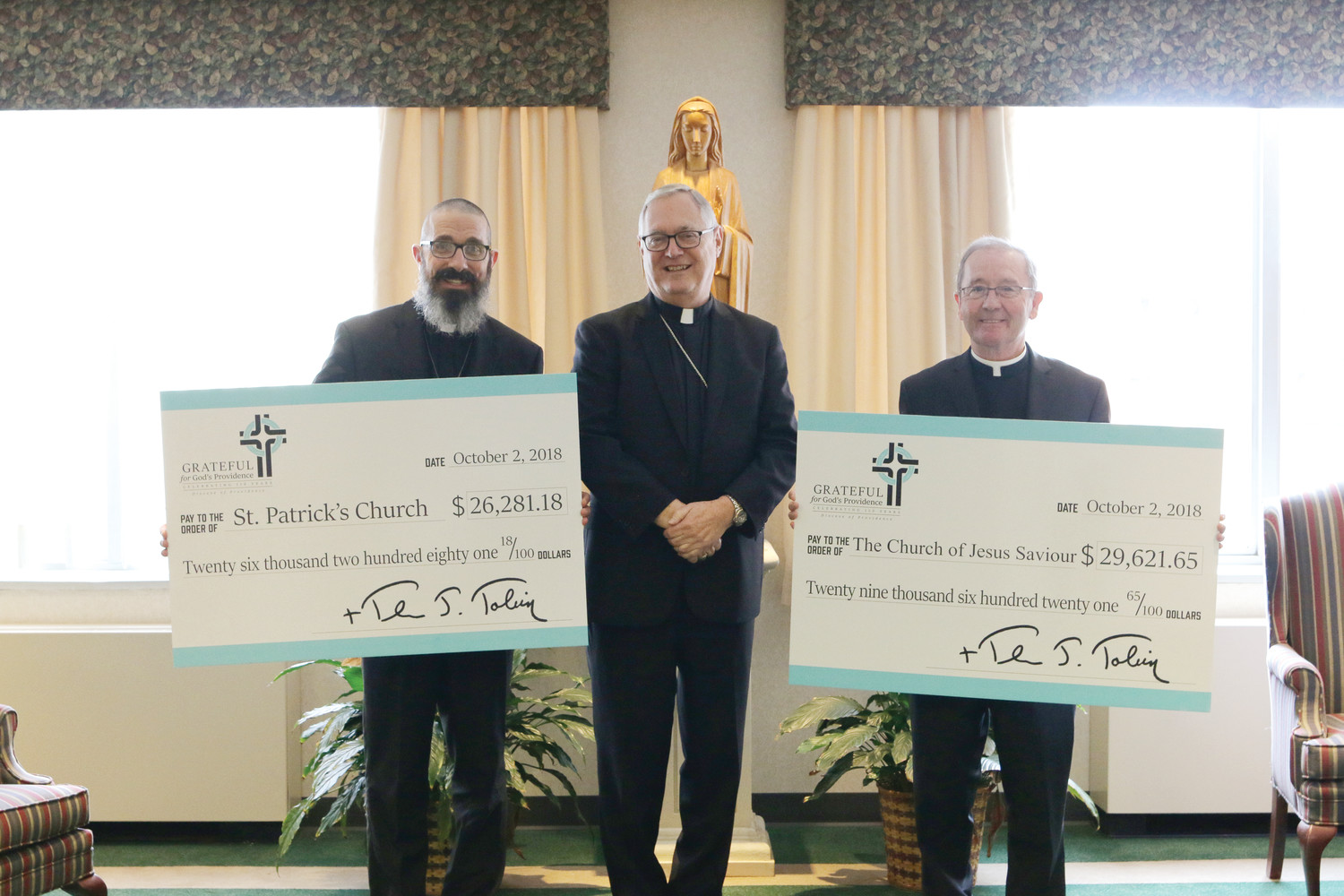 Bishop Thomas J. Tobin presents two separate checks to Father James Ruggieri, pastor of St. Patrick Church, Providence, at left, and to Father Francis O’Loughlin, pastor of Jesus Saviour Church, Newport. As part of the Grateful for God’s Providence Campaign, each parish in the diocese has a campaign fundraising goal, and receives back 40 percent of the money collected toward that goal. If a parish exceeds its goal, it receives 60 percent of those funds.