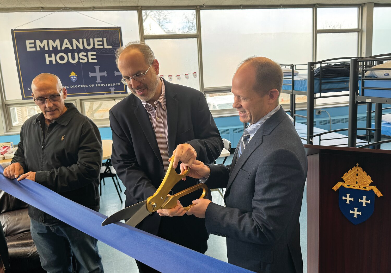 State Housing Secretary Stefan Pryor, center, assists Jim Jahnz, secretary of Catholic Charities and Social Ministries, in cutting the ribbon marking the official opening of the new women’s shelter Emmanuel House, as Shelter Manager Mike Marzullo looks on.